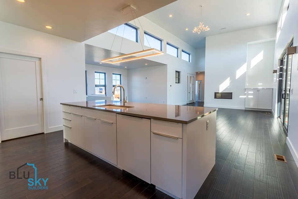 Modern kitchen with island, white cabinets, dark wood floors, and high ceilings.