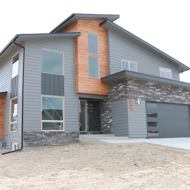 Modern gray house with wood and stone accents, large windows, and a gray garage door.