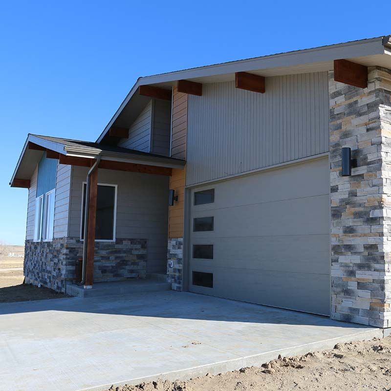 Modern house with stone and wood accents, gray siding, and a garage door, under a blue sky.