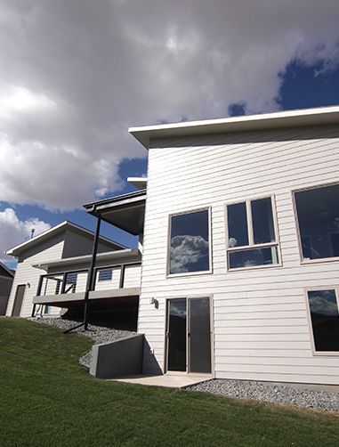 Modern white house with large windows, grass slope, and cloudy blue sky.