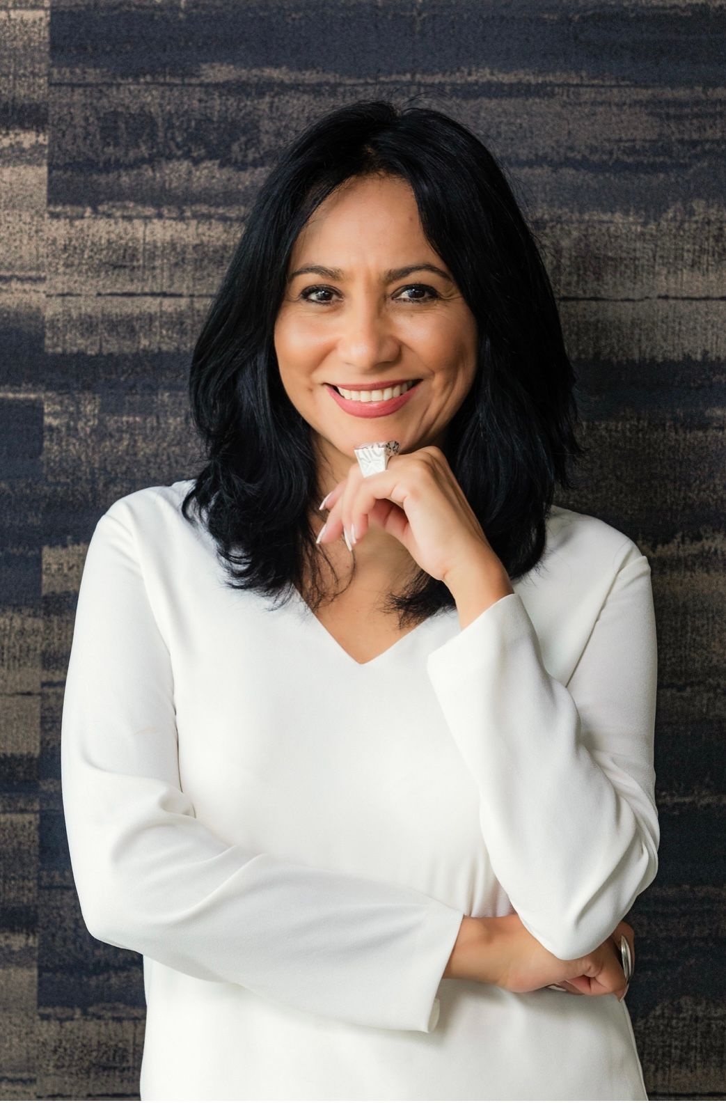 Smiling woman in a white top posing with her hand under her chin against a dark textured background