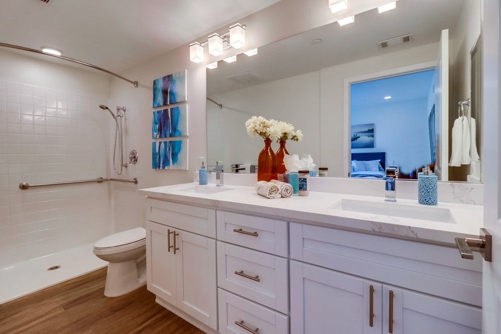 Bathroom with white cabinets, double sink, and a shower with grab bar.