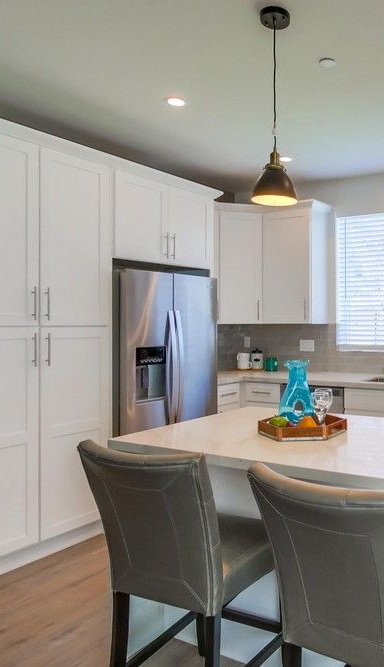 Modern white kitchen with island, stainless steel appliances, and pendant lights.