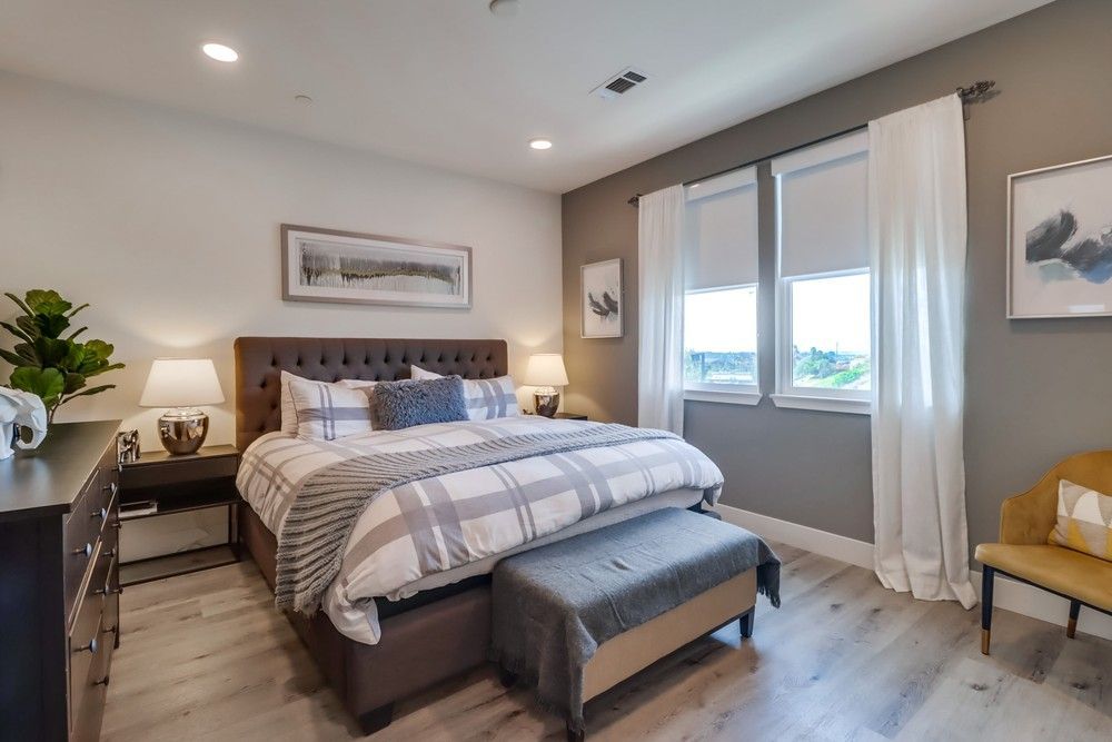 Bedroom with a brown tufted headboard, plaid bedding, gray walls, and light wooden floor.