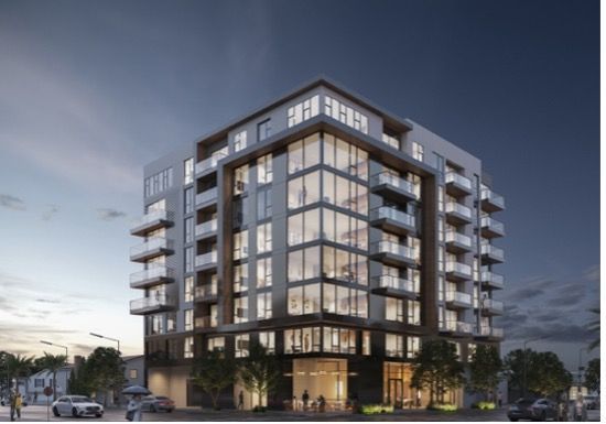 Woman with dark curly hair smiling. Wearing a light brown top.