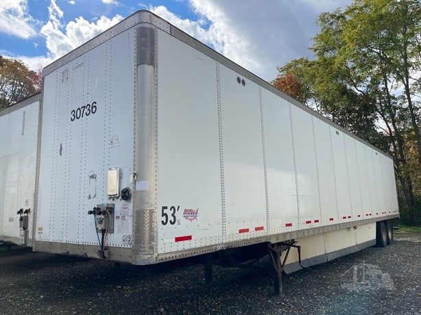 White semi-trailer parked outdoors with side panels and red striping. 