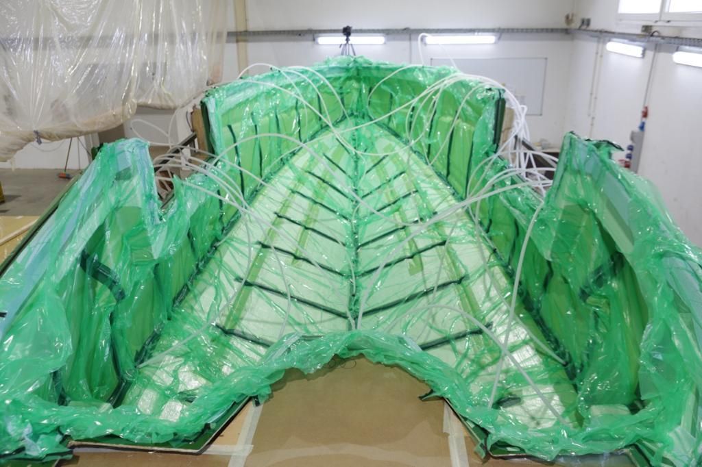 Large green-wrapped structure, possibly a boat hull, in a workshop setting.
