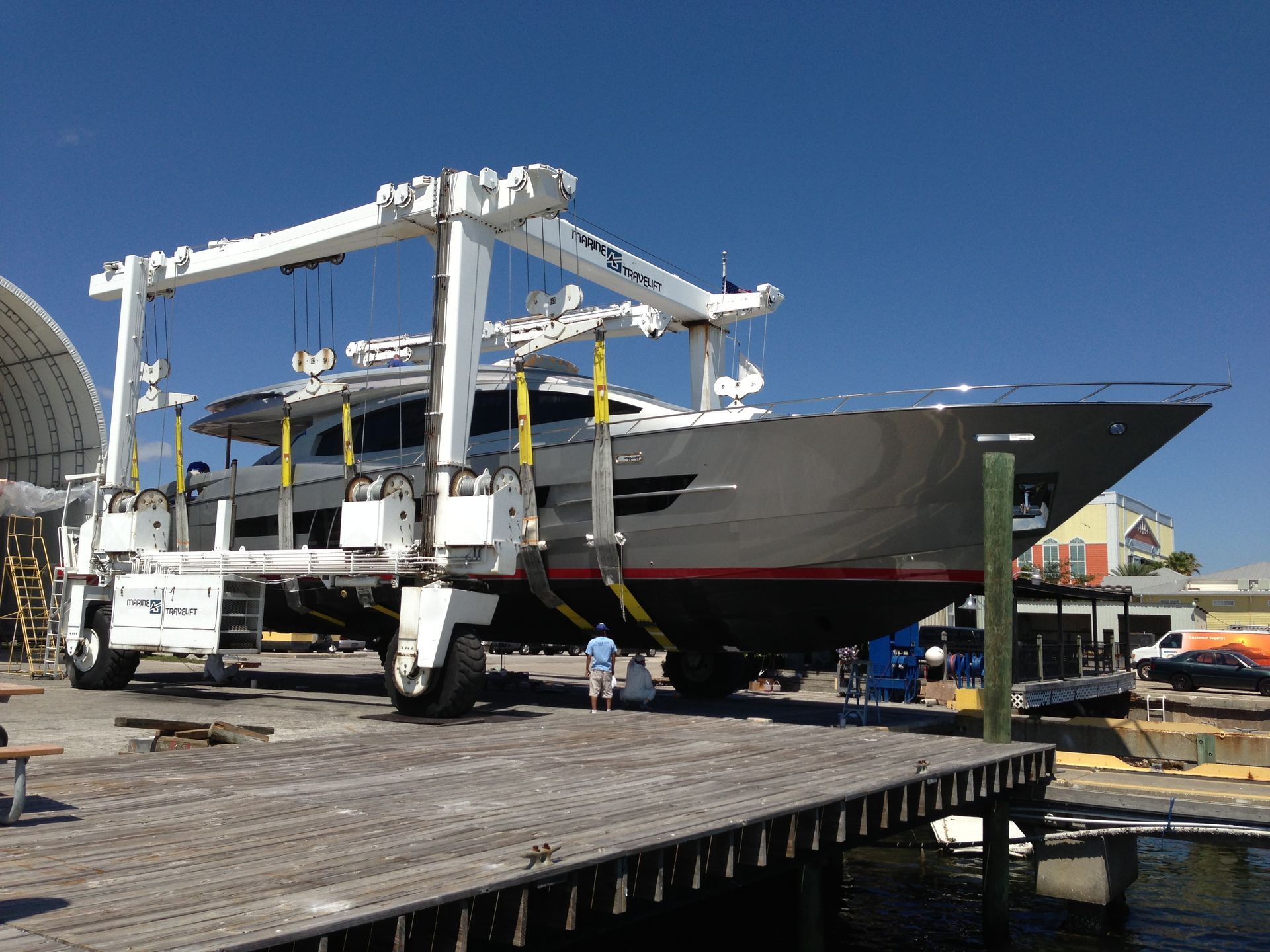A large yacht being lifted by a boat hoist on a dock, bright blue sky overhead.