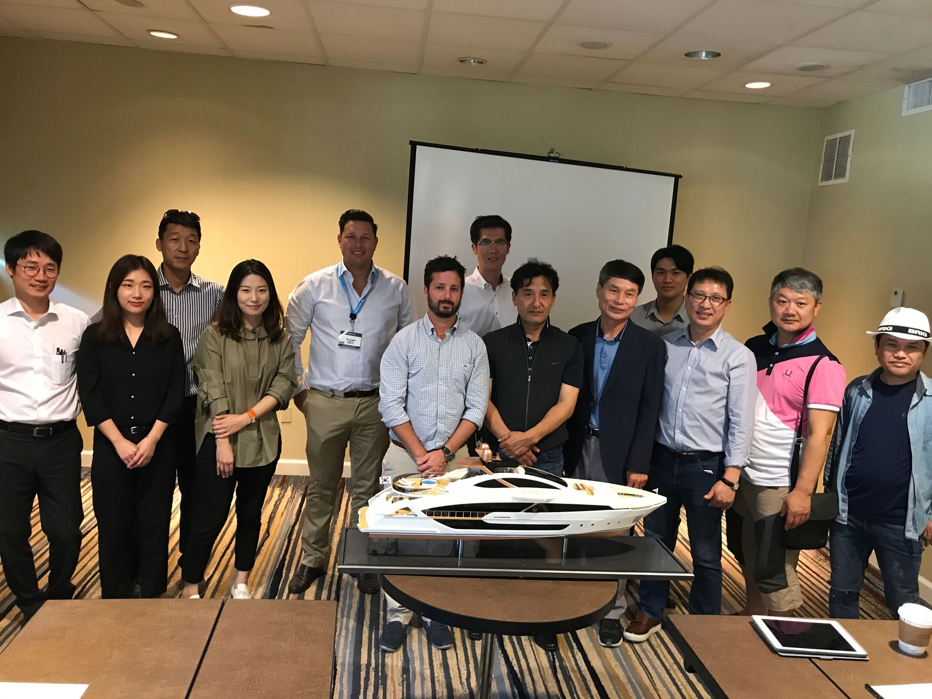 Group of people posing with a boat model in a conference room. Some are smiling.