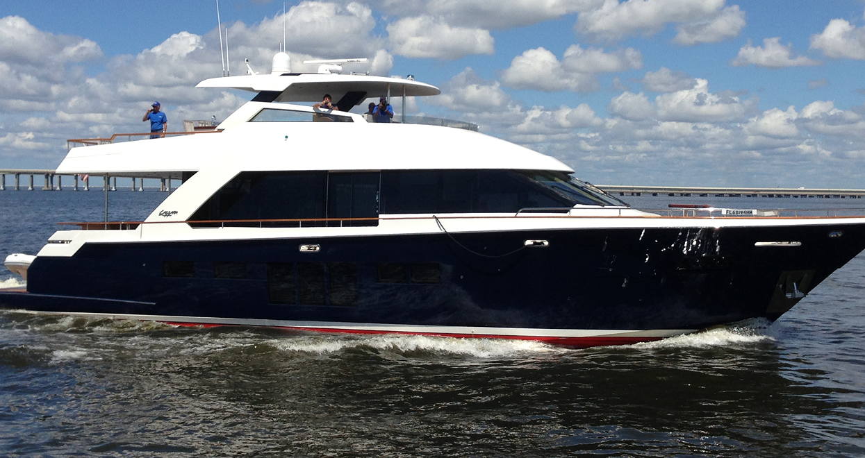 Blue and white motor yacht sailing on water, two people on deck under a blue sky.