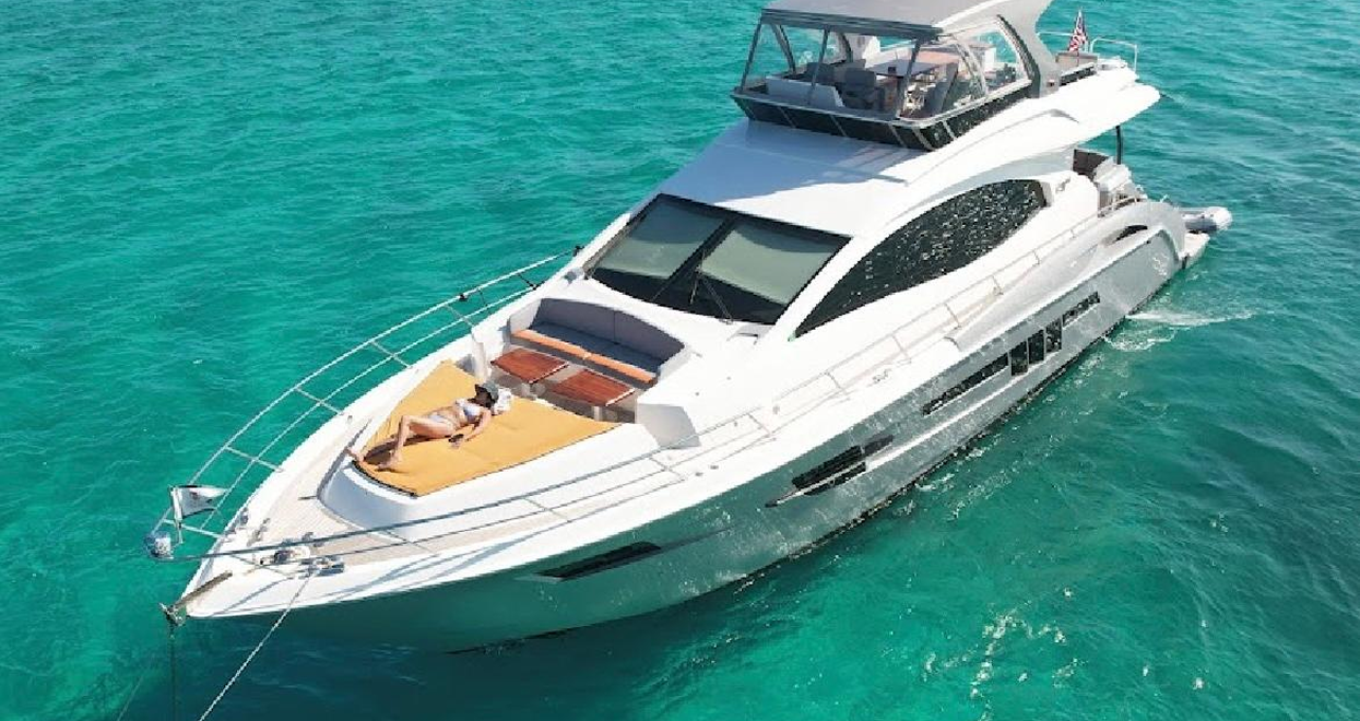 A white motor yacht on turquoise water, with a sunbathing deck, and a flybridge.