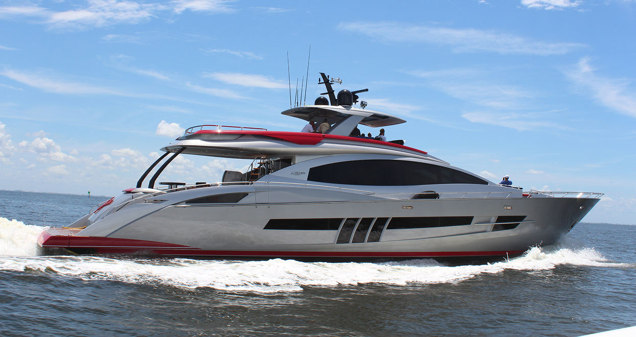 A sleek silver and red yacht sailing on blue water under a bright, cloudy sky.