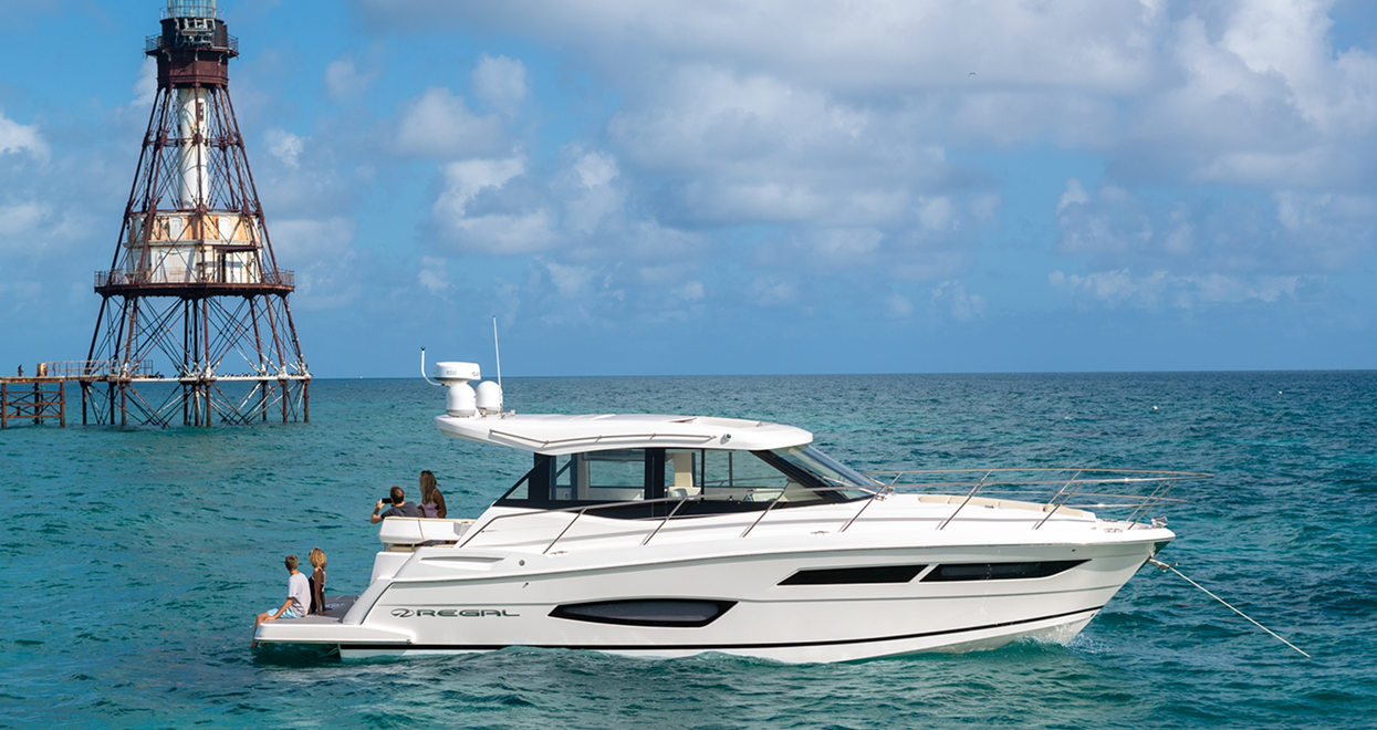 White yacht cruising in turquoise water near a metal lighthouse.