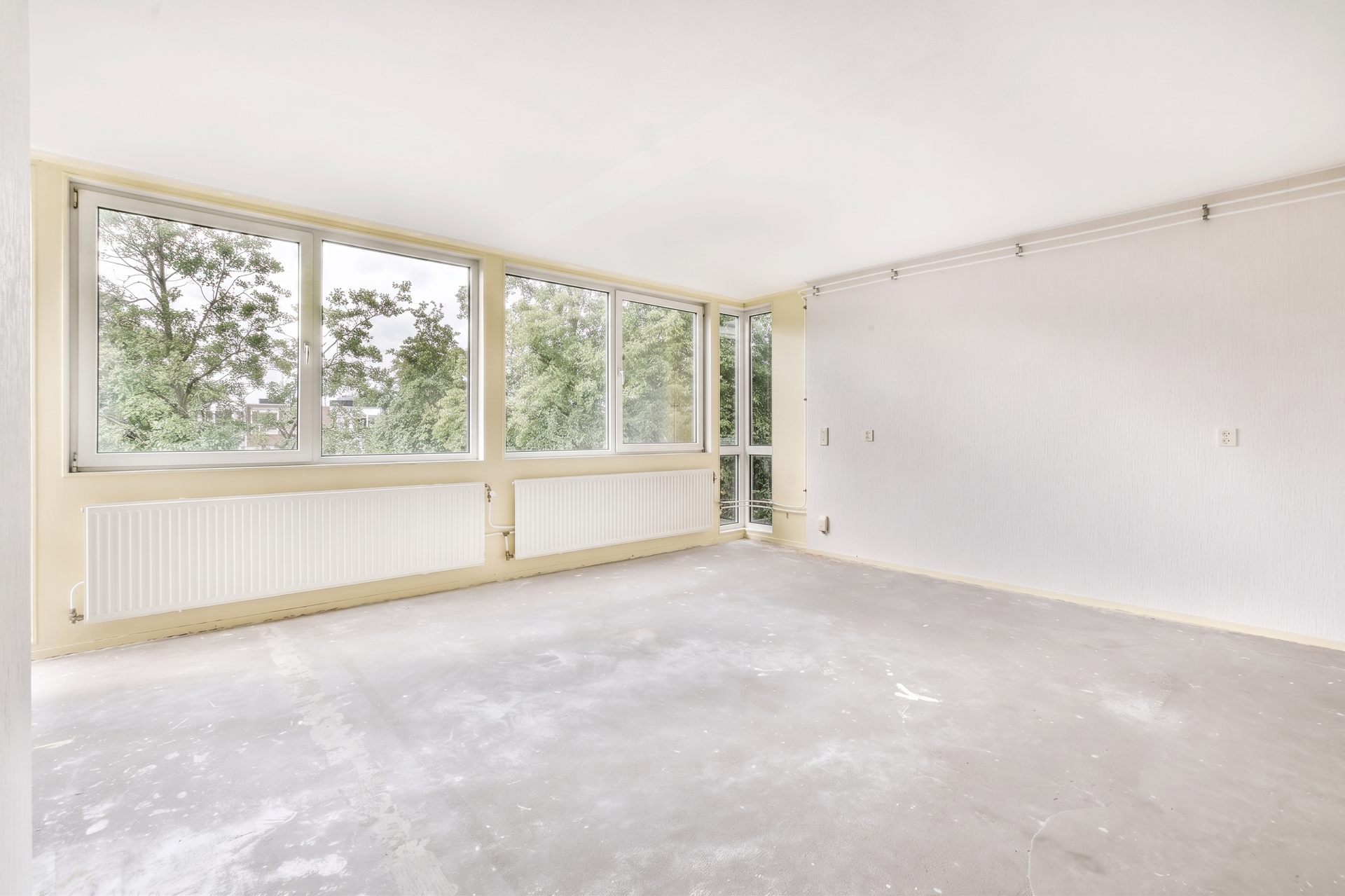 Empty bright room with large windows, white walls, and unfinished carpeted floor
