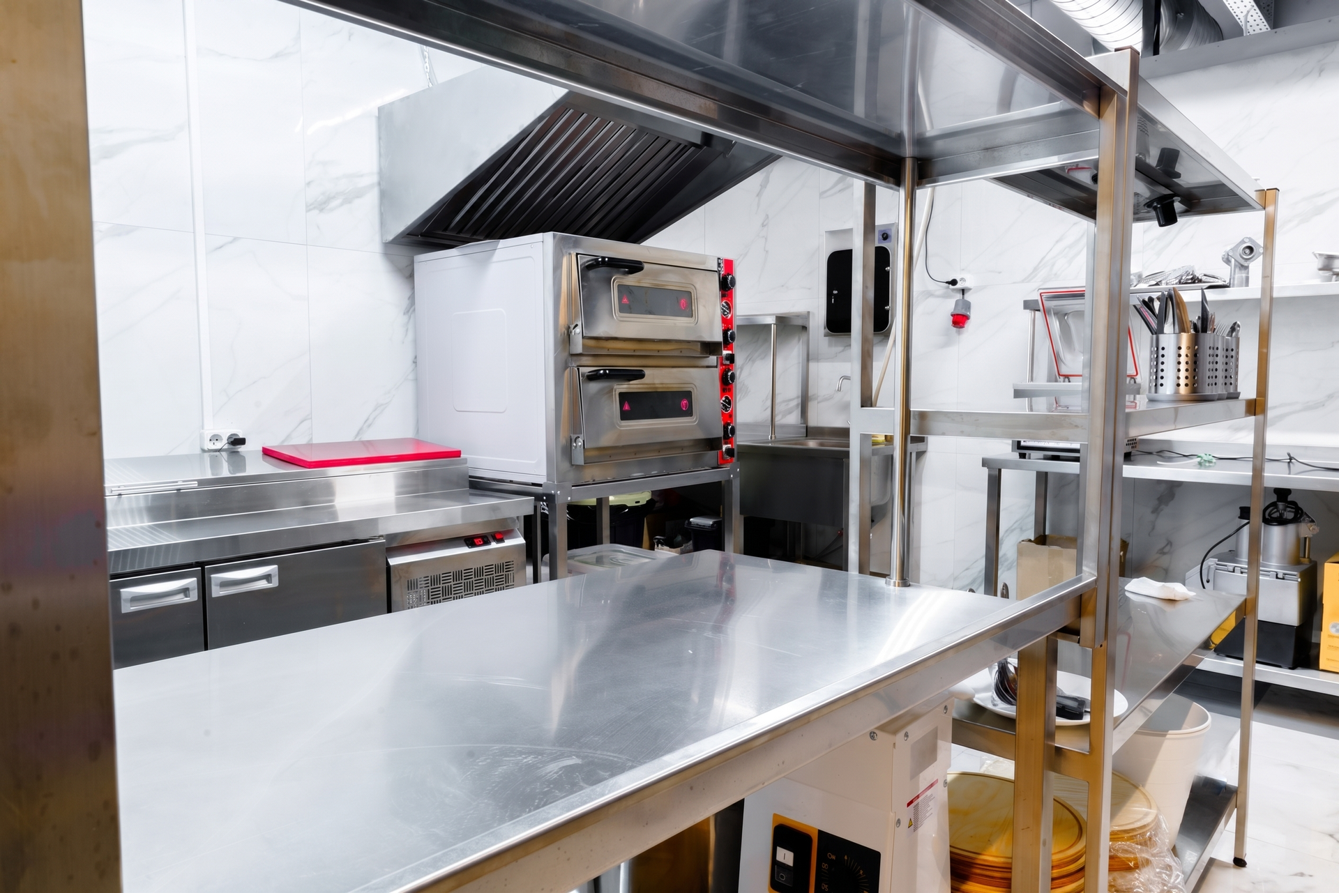 Stainless steel kitchen with ovens, prep counters, and cooking equipment under a hood