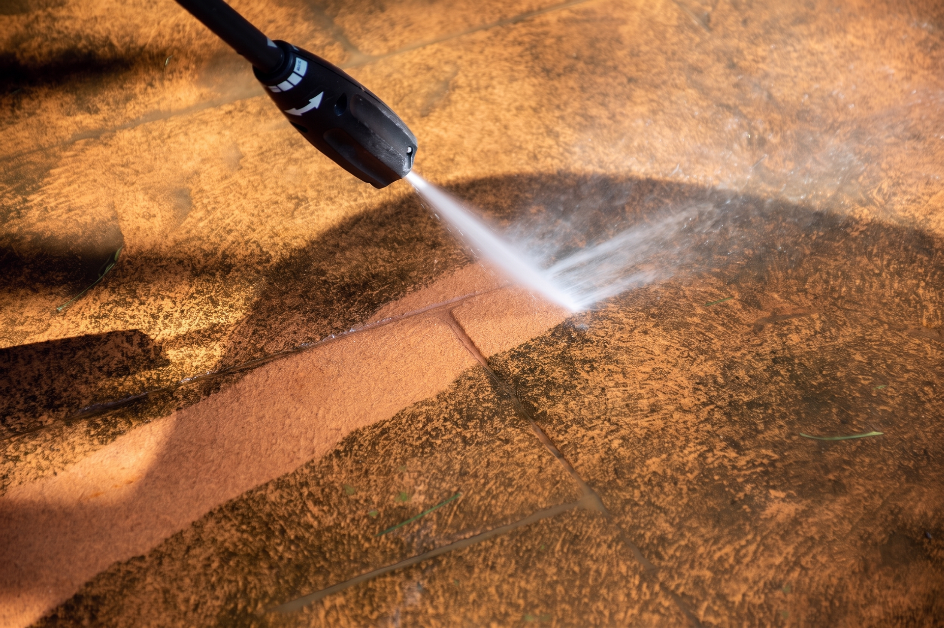 Pressure washer spraying water over a sandy surface, creating a clean diagonal strip