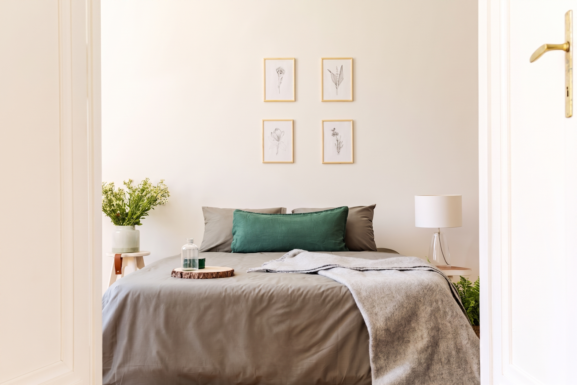 Cozy bedroom with beige walls, neatly made bed, framed wall art, and a small lamp by the side table