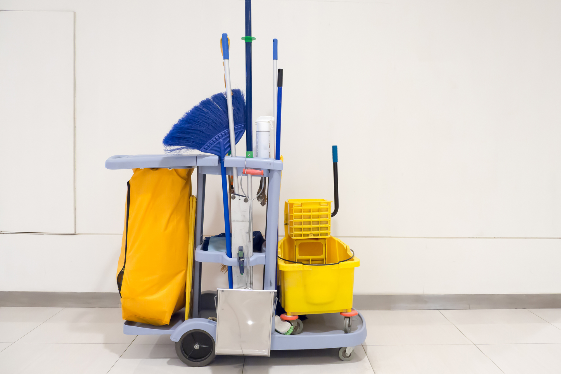 Cleaning cart with mop, broom, bucket, and yellow supplies in a tiled hallway