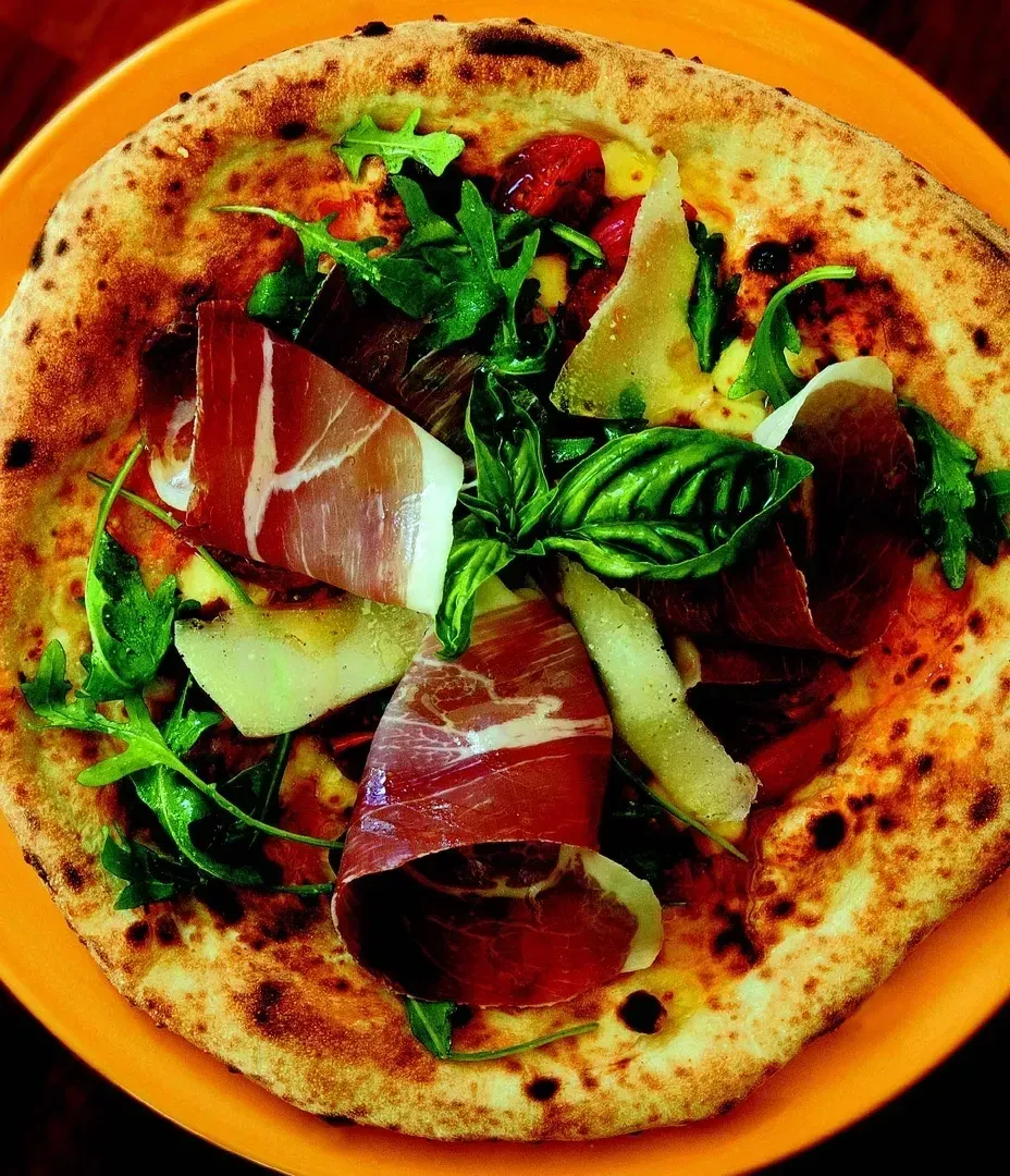A pizza with meat and vegetables on an orange plate