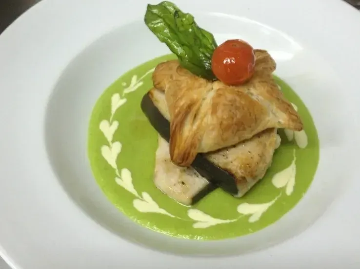 A plate of food with a green sauce and a tomato on top