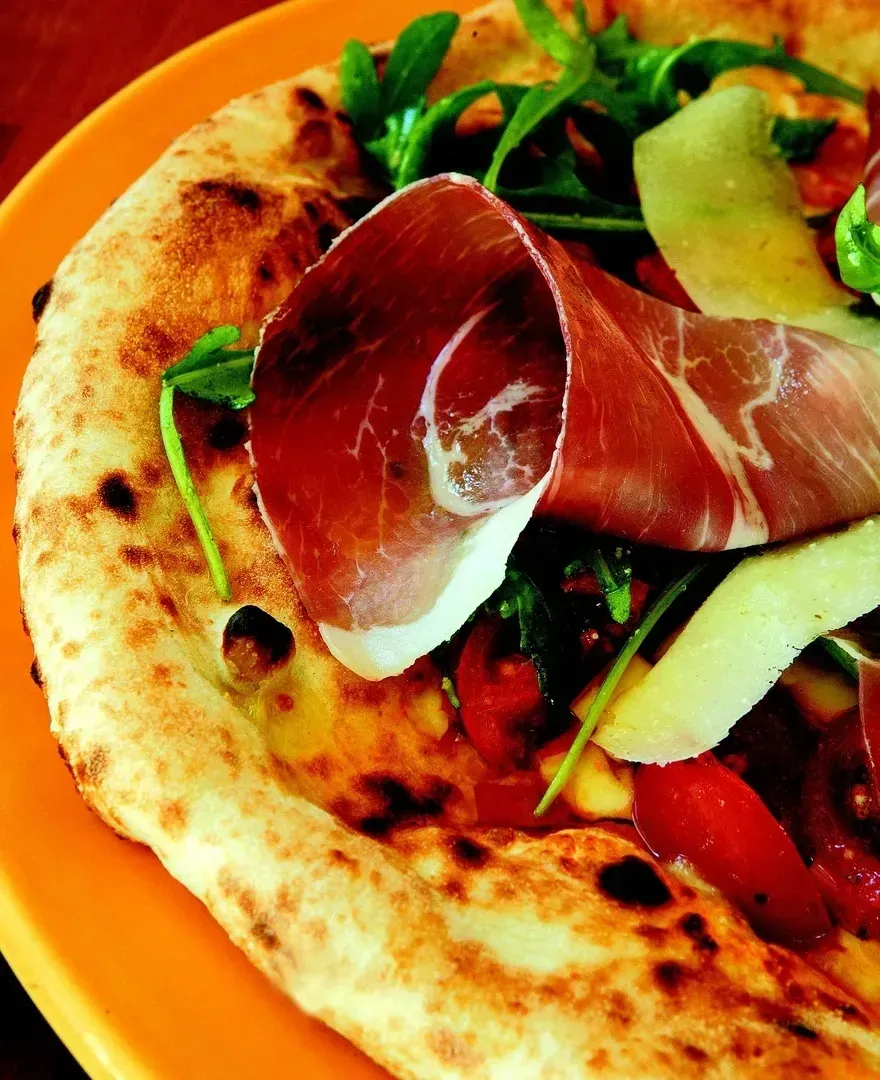 A pizza with meat and vegetables on an orange plate