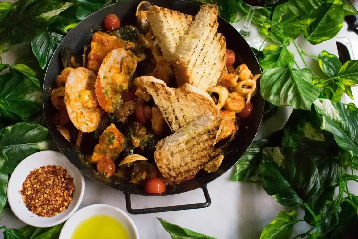 A pan filled with seafood and bread on a table surrounded by leaves.