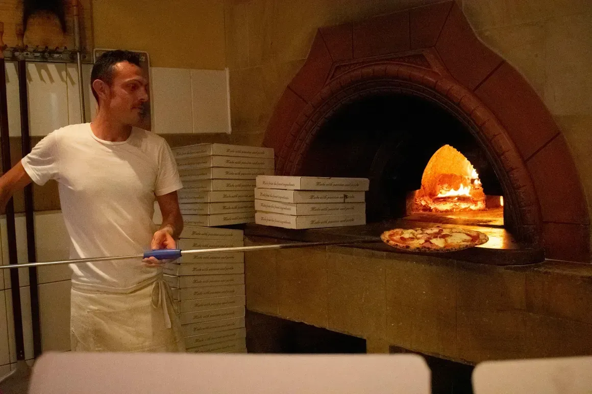 A man is putting a pizza into a pizza oven