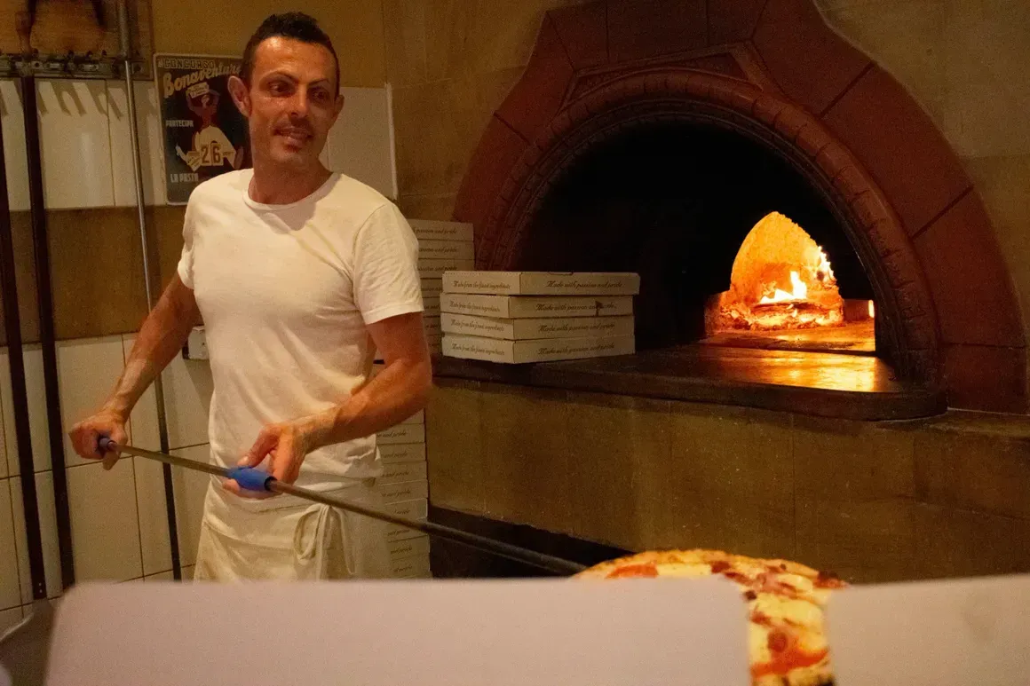 A man is putting a pizza into a pizza oven
