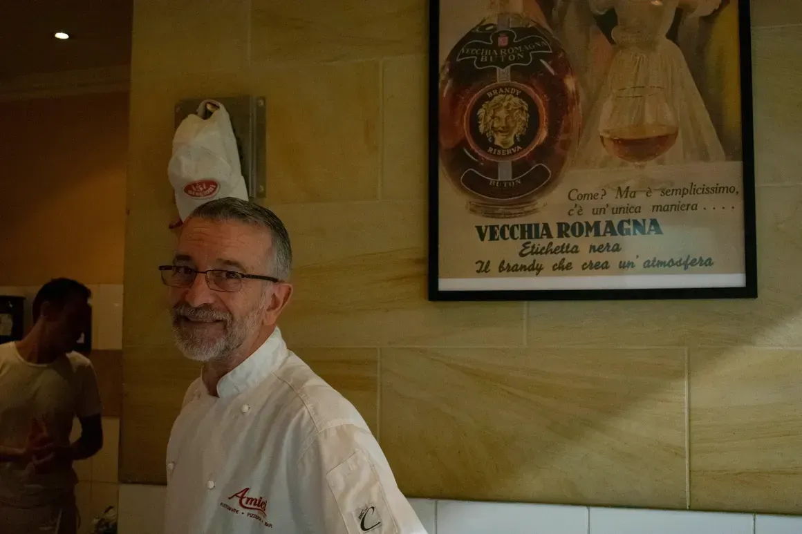 A man with glasses and a beard is standing in front of a sign that says vega romagna