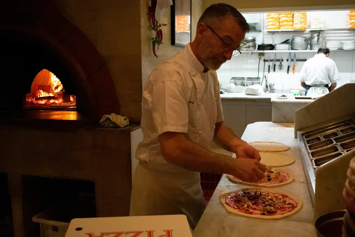 A man is preparing a pizza in front of a pizza box that says pizza