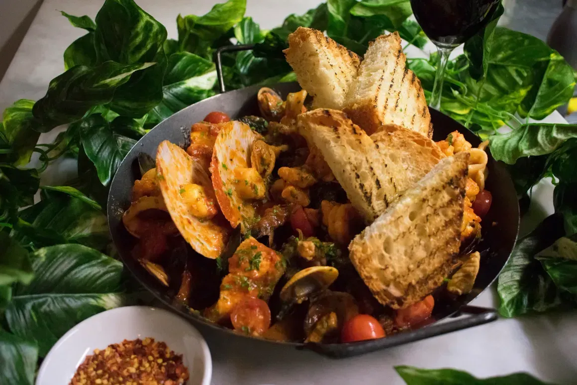 A pan of food with bread and a glass of wine on a table.