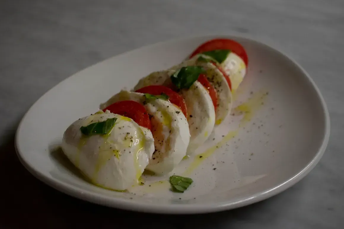 A white plate topped with mozzarella and tomatoes on a table.
