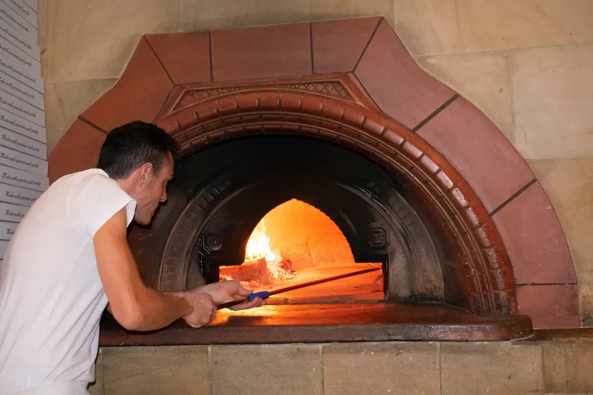A man is putting a pizza into a pizza oven