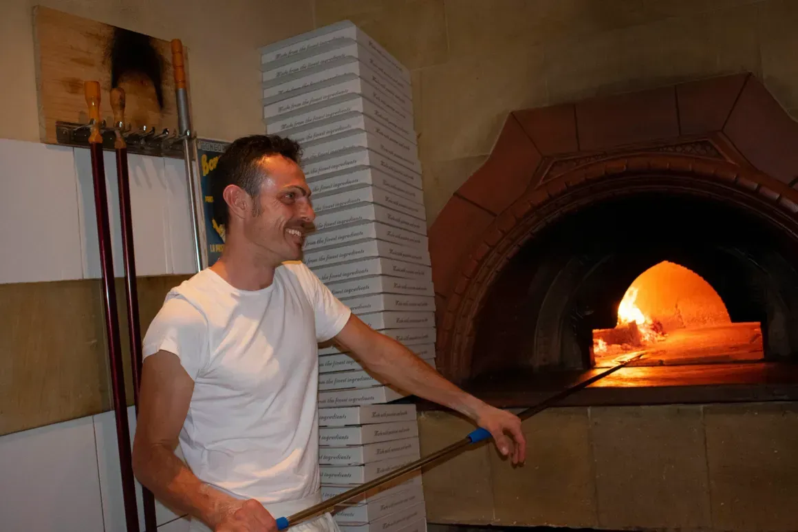 A man is standing in front of a pizza oven.