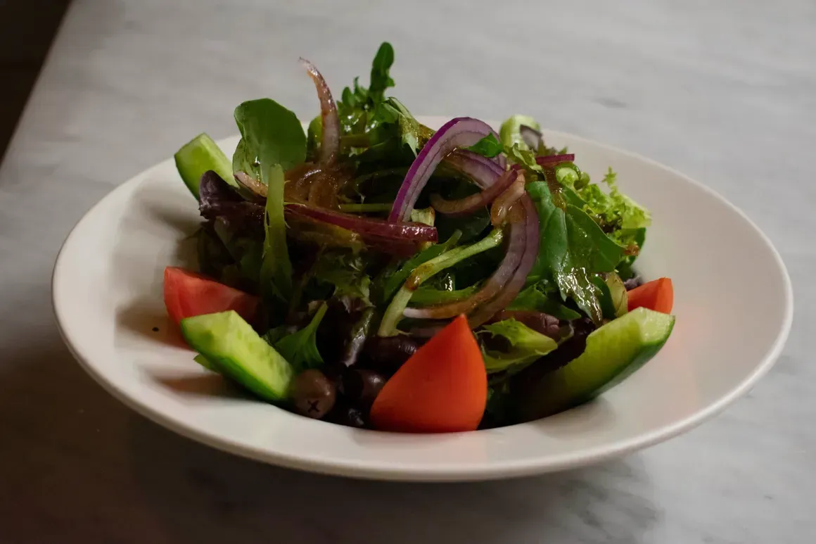 A salad with tomatoes , cucumbers , onions and olives in a white bowl on a table.