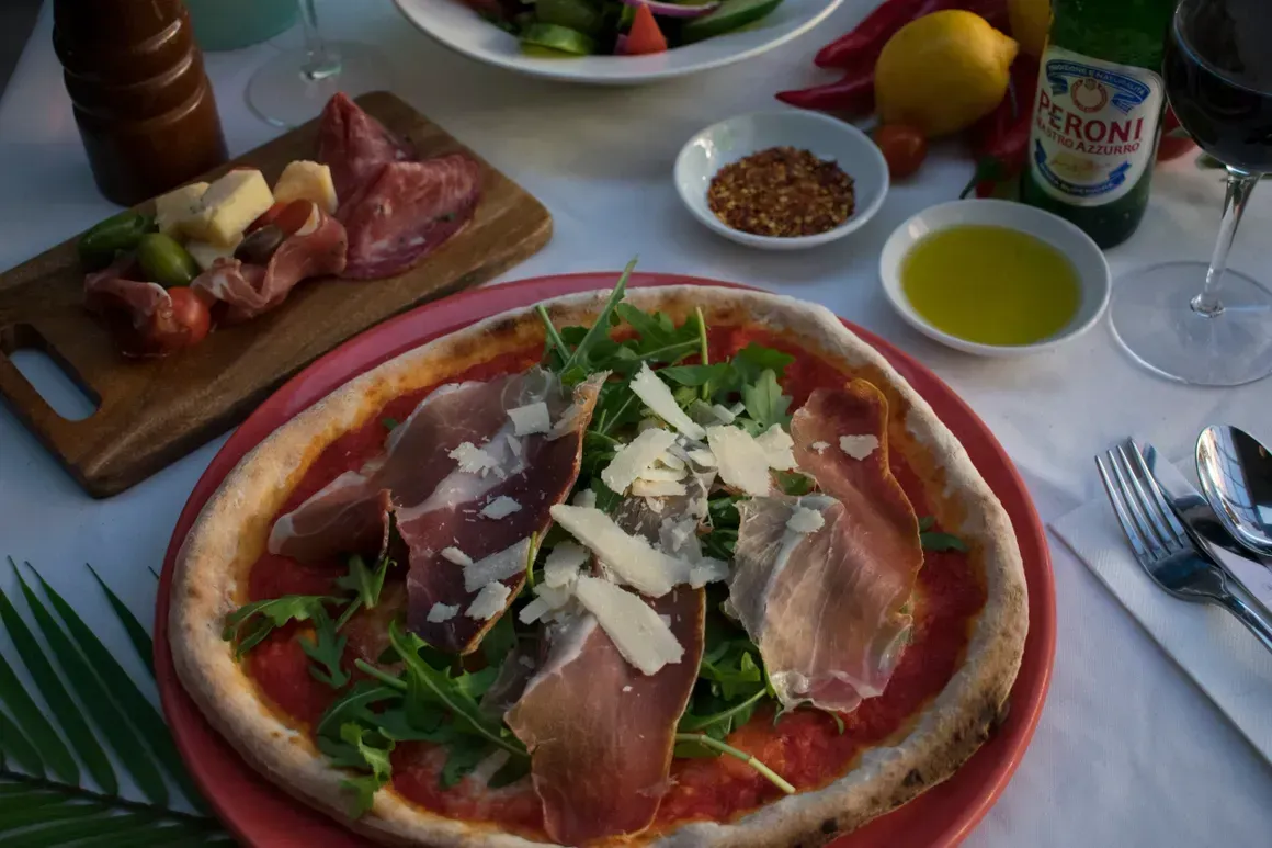 A pizza on a plate with a bottle of limoni in the background