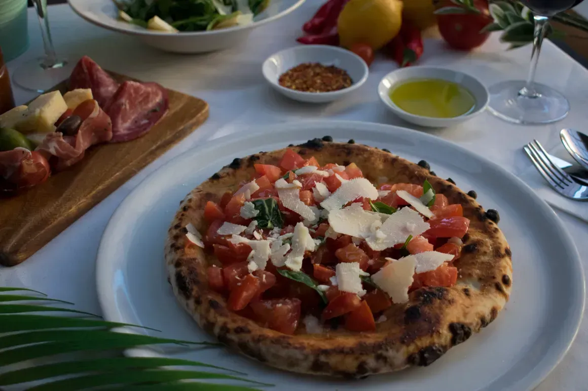 A pizza with tomatoes and cheese is on a white plate on a table.