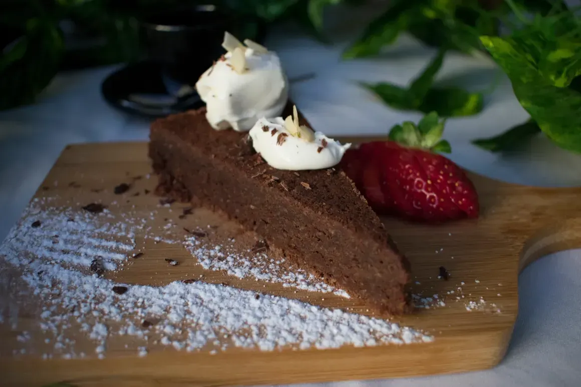A piece of chocolate cake with whipped cream and strawberries on a wooden cutting board.