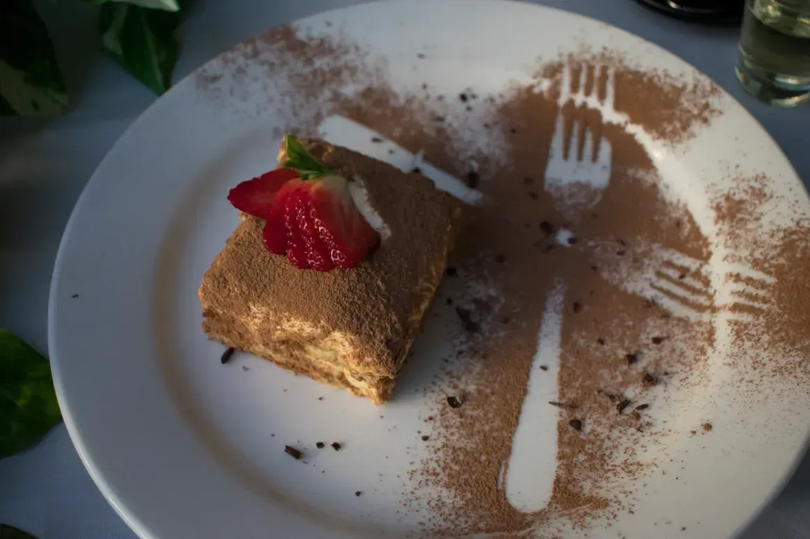 A white plate topped with a piece of cake and a strawberry on top.
