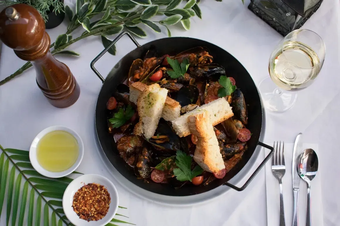 A pan of food with bread and a glass of wine on a table.