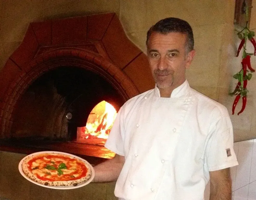 A man is holding a pizza in front of an oven