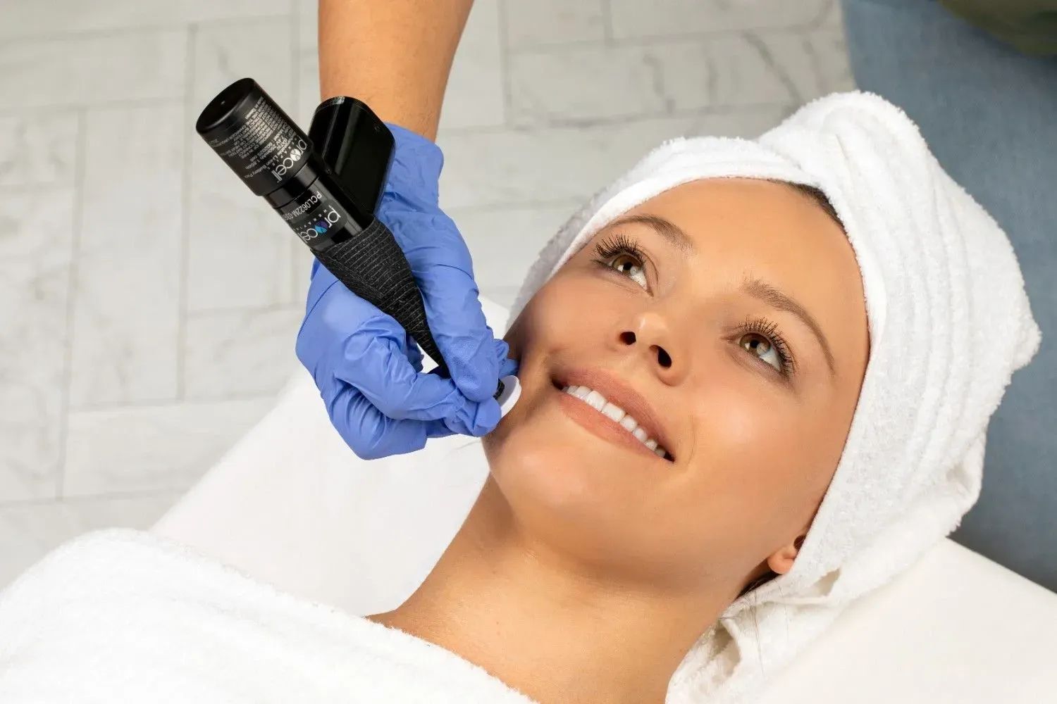 Woman receiving cosmetic facial treatment, smiling. Spa setting, gloved hand with device.
