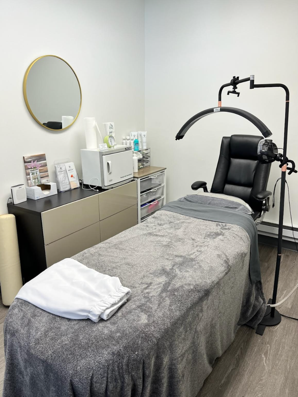 A treatment room with a bed, chair, and equipment for beauty services.
