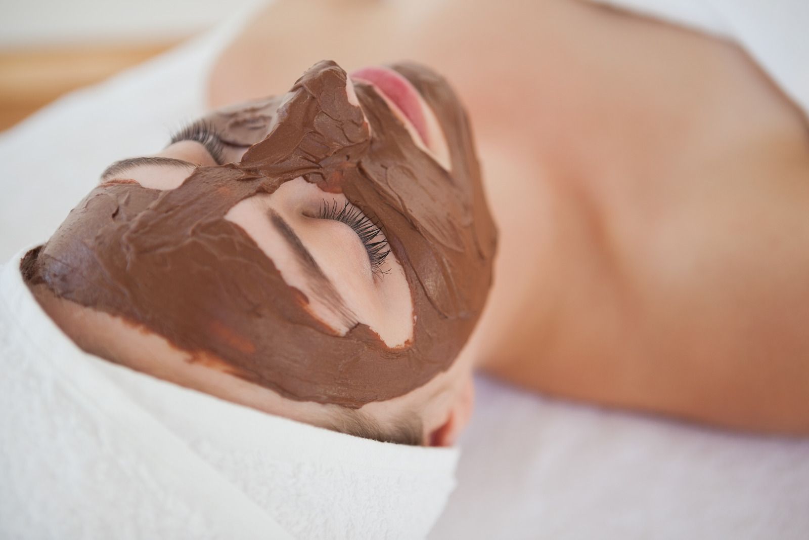 A woman is laying on a bed with a chocolate mask on her face.