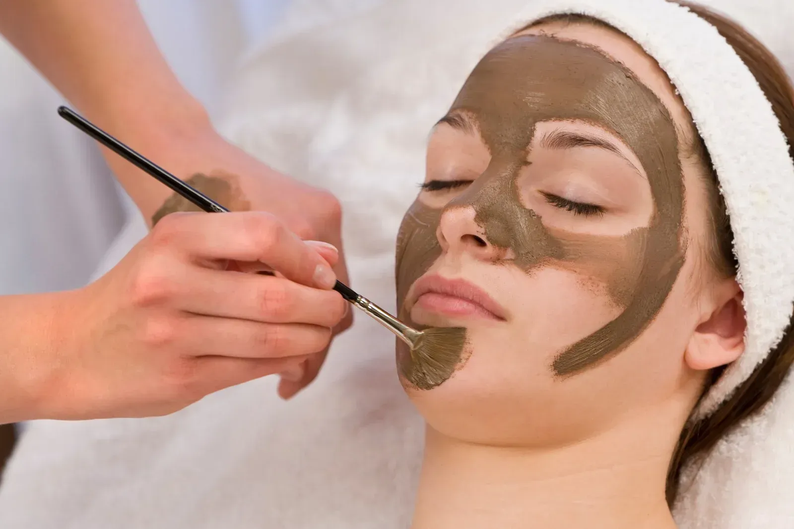 A woman is getting a clay mask on her face