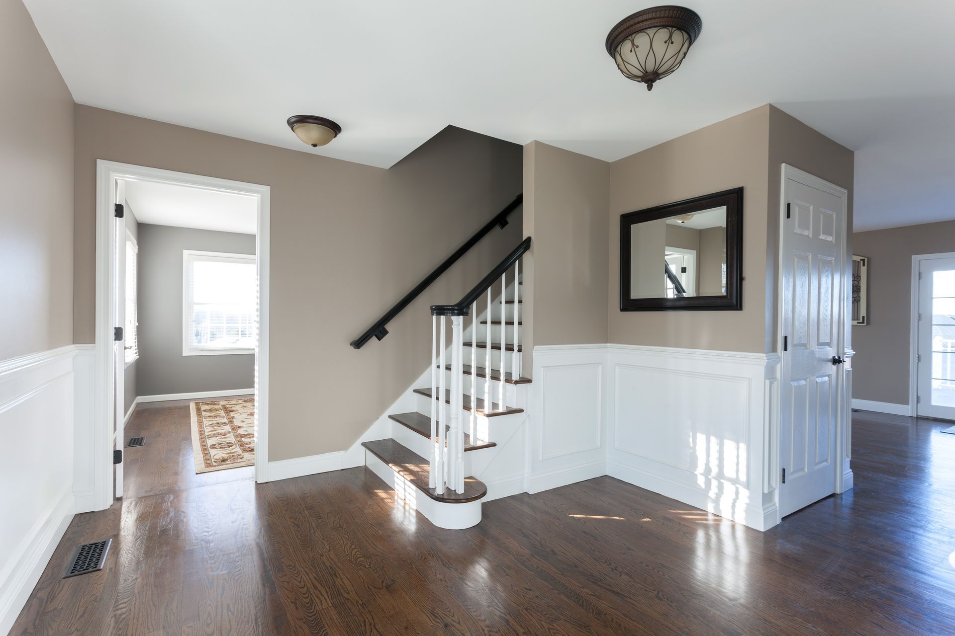 Entryway with staircase, dark wood floor, white wainscoting, brown walls, mirror, and two light fixtures.