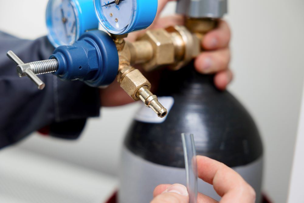 A Person is Holding a Hose in Front of a Gas Cylinder — FC Gas Fitting in Maryborough, QLD