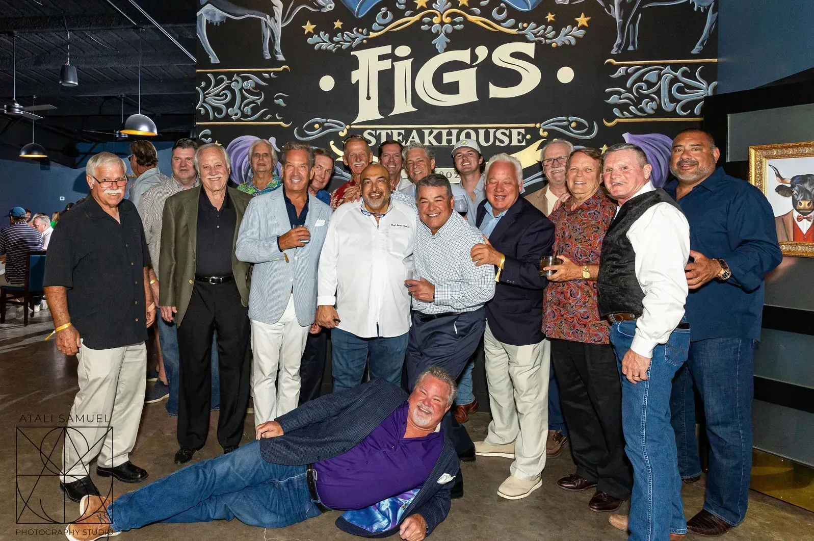 Group of men posing at Fig's Steakhouse. One man is on the floor, others are smiling, a sign is in the background.