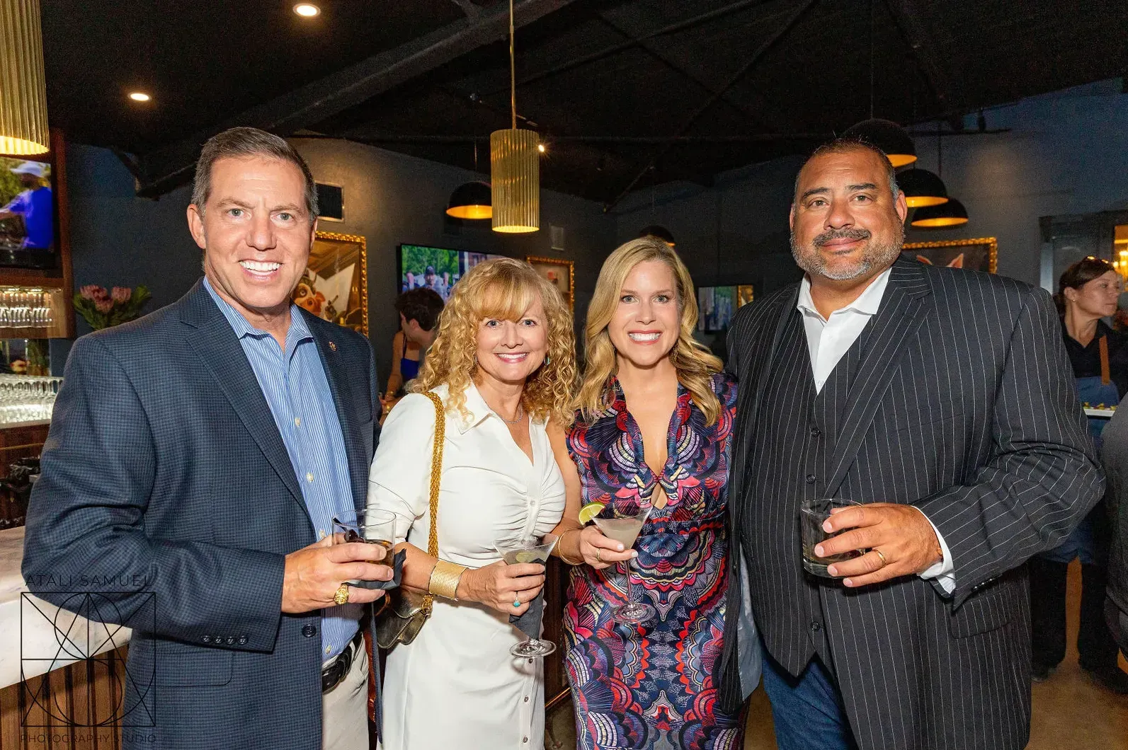Four people, two men and two women, smiling at a social gathering. Dark setting with drinks.