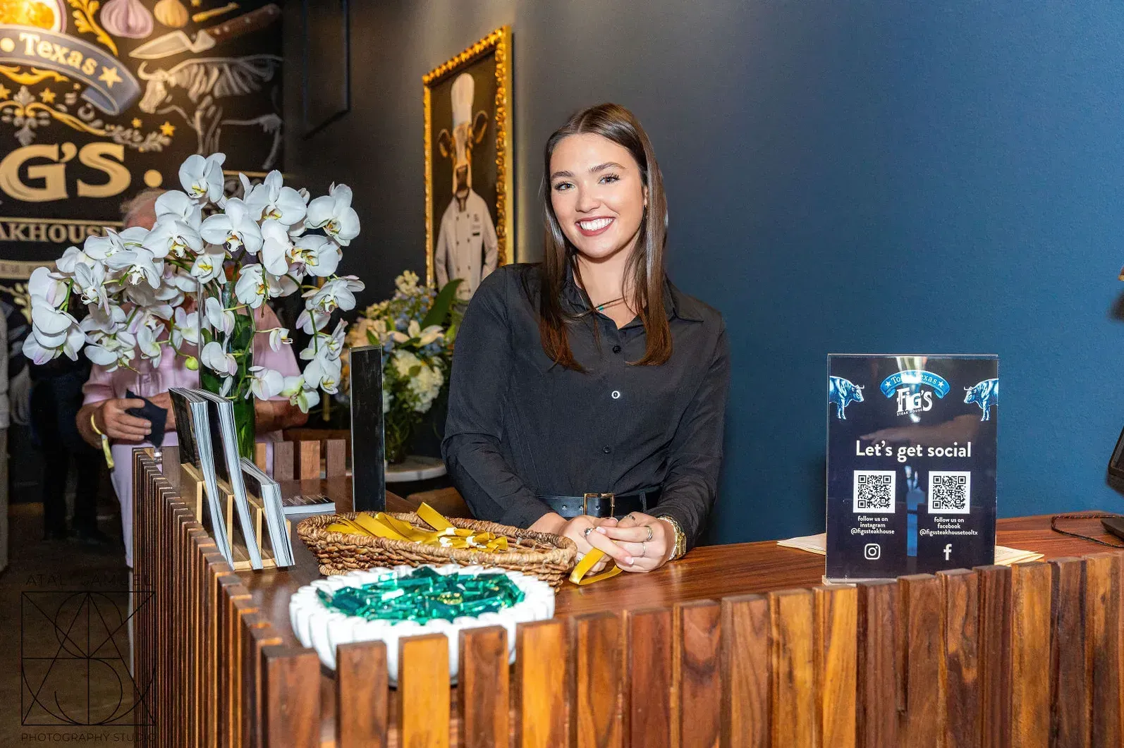 Woman at a wooden counter with flowers and food samples in a restaurant; blue wall backdrop.